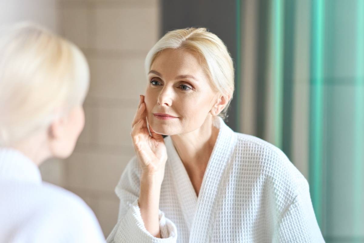 Older woman staring at reflection while touching her face.